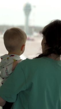 Anne ve oğlu havaalanında uçağa bakıyorlar. Uçağa binmek ve uluslararası terminalde seyahat etmek için bekliyor. Dikey Çekim.