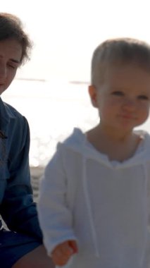 Küçük çocuk kumsalda annesinden kameraya doğru yürüyor. Annem ve okyanus arkada. Dikey Çekim.