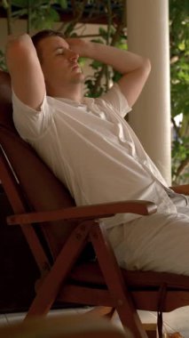 Bir adam Hint Okyanusu 'nun kıyısında gözlüklü bir sandalyede dinleniyor. Tropikal bir adada dikey çekim yaparken uyku molası konsepti.