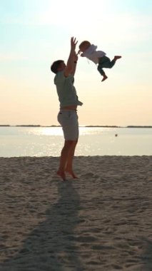 Baba, bir buçuk yaşındaki oğlunu kapı kollarından tutup fırlatıyor ve sonra da onu yakalıyor. Maldivler Sahili 'nde mutlu bir aile tatilcisinin eğlenceli akrobatik numarası..