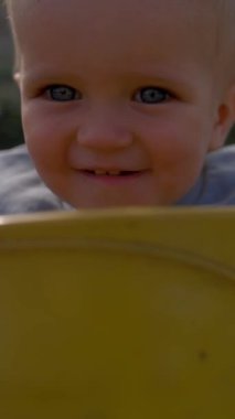 Neşeli çocuk bulanık arka planda salıncaklara biniyor. Sarışın çocuk, güneşli bir günde çocuklar için çocuk parkında etkinlikten hoşlanıyor. Yavaş çekim, dikey çekim..