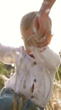 Toddler, anne 'nin parlak güneş ışığı altında çayırlarda yürümesini tutuyor. Sarışın çocuk kırsalda güneşli bir günün keyfini çıkarıyor. Yavaş çekim dikey çekim..