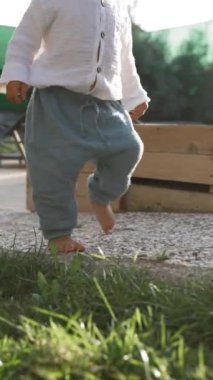 Küçük çocuk gün batımında kır evinin bahçesindeki yumuşak yeşil çimlerde yalınayak yürüyor. Tatlı çocuk yaz tatilini yavaş çekimde, dikey çekimde geçiriyor..