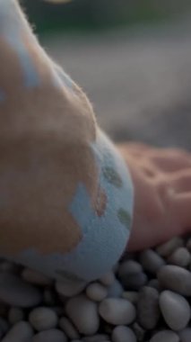 Bir avuç çocuk kumsalda bulanık arka planda duran çakıl taşlarını yakalıyor. Küçük çocuk deniz kıyısında oturuyor ve tatilin tadını çıkarıyor. Aşırı yakın çekim yavaş çekim dikey çekim..