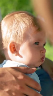 Küçük oğlan babasının yanına oturup surat asıyor. Baba oğlunu büyük bir eliyle okşar. Yürüyen çocuk park alanını dikkatli ve eğlenceli bir ifadeyle dikey çekim yaparak inceliyor.