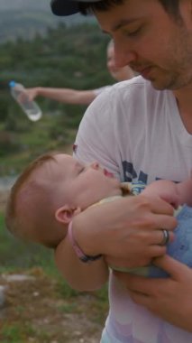 Babası kucağında bir şişe suyla kucağında annesiyle kucağında küçük bir kızı sallıyor. Çocuklu genç bir aile doğayı araştırıyor. Yavaş çekim, dikey çekim..