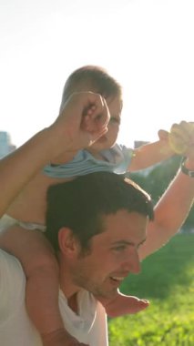 Mutlu baba, güçlü omuzları olan tatlı bir kızla oynuyor. Kızı, parkın yakın çekim dikey çekimine karşı yüzünde ciddi ve eğlenceli bir ifadeyle etrafına bakıyor..