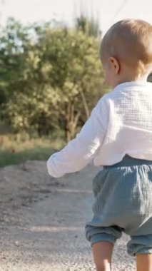 Sevimli küçük çocuk, güneşli bir günde yemyeşil yollarda gülerek koşuyor. Sarışın çocuk yaz tatilinin tadını çıkarıyor. Yavaş çekim dikey çekim..