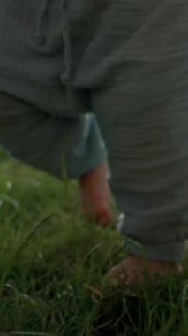 Tatlı çocuk bahçede elinde sopayla büyüyen yemyeşil çimlerde yalınayak yürüyor. Yürüyen çocuk yaz günü hafta sonunu kırsalda yavaş çekimde dikey çekimde geçirir..