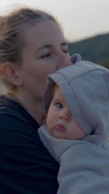 Anne, alacakaranlıkta kumsalda karanlık dağlara karşı duran sevimli küçük bebeği kollarında tutuyor. Saçı topuzlu ve çocuklu bir kadın yürüyordu. Ağır çekim, dikey çekim..