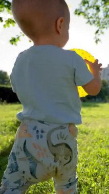 Küçük çocuk gün ışığında ailesine doğru yürürken topu tutuyor. Güneşli bir günde çimenlerde koşan çocuk gülümser ve güler. Çocuk, anne babasıyla pikniğe gitmekten hoşlanıyor..