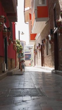 Anne ve oğlu, güneşli bir günde eski binalarla dar gölgeli caddelerde yürürler. Kadın ve küçük çocuk antik turistik kente yaz yolculuğunun keyfini çıkarıyorlar..