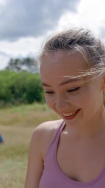 Genç bayan çayırdaki çadırda temiz havada çalışmaktan hoşlanıyor. Kahverengi saçlı çalışan, dijital cihazla bilgi yazıp ararken dikey çekimde gülümsüyor..