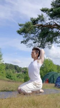 Siyah saçlı yürüyüşçü çayırdaki kamp çadırları tarafından çimlerin üzerine konulmuş minder üzerinde yoga yapıyor. Güneş ışığı sporcunun güçlü vücudunu aydınlatır. Genç adam, Dikey Vuruş Ormanı 'nda hafta sonunun keyfini çıkarıyor.