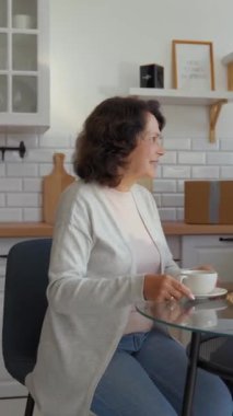 Kıdemli erkek ve kadın, yeni evdeki mutfak masasında oturarak sıcak çay içiyorlar. Üniformalı kurye yaşlı çiftlere ağır karton kutular taşımada yardım ediyor..