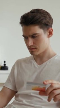 Adam kredi kartı bilgilerini dizüstü bilgisayarla internet sitesinde tutuyor. Genç müşteri çevrimiçi dükkandan alışveriş yapıyor. Evdeki sandalyeye oturup dikey çekim yapıyor..