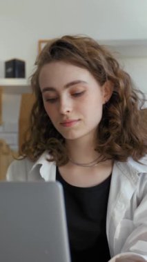 Genç bir kadın yeni daireye taşındıktan sonra çalışmak için zaman ayırıyor. Kadın serbest çalışan, mutfak masasında karton kutulara karşı dikey çekim yapan bir cihaz kullanıyor..