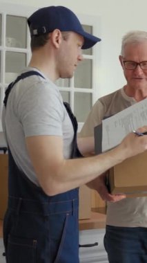Kurye, yaşlı çiftin yeni dairesine konformasyon kağıdı imzalamak için karton kutu getiriyor. Gözlüklü yaşlı gri saçlı adam, içinde dikey çekimler olan bir kutu alır..
