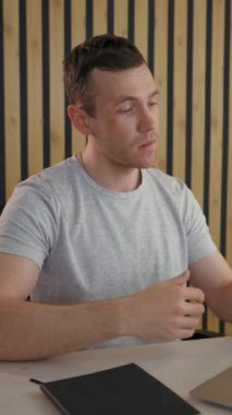 İşadamı, müşterisiyle bilgisayar aracılığıyla video görüşmesi yapıyor. Genç adam, modern ofis odasındaki parlak lambanın yanında oturan anlaşmadan bahsediyor..