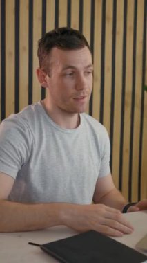 Genç çalışan, parlak lambanın yanındaki masada dizüstü bilgisayarla iş arkadaşıyla görüntülü konuşma yapıyor. İnsan çevrimiçi iletişim için modern aygıt kullanır. Dikey Vuruş.