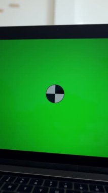 Adam yeşil renkli ekranlı dizüstü bilgisayardan kursları izliyor. Modern elektronik cihaz ofis yakınındaki beyaz masanın üzerinde dikey çekim yapıyor.