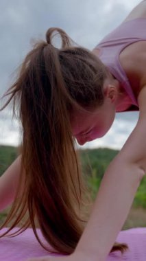 Genç kadın yeşil tepede yoga pozu veriyor. Spor giyim sektöründeki atletik kadın bulutlu gökyüzüne karşı Asana Upward-Facing Dog 'a odaklanıyor..