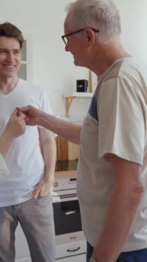 Yaşlı baba ve anne genç evli çifte yeni bir daire hediye etti. Mutlu erkek ve kadın anahtarı alır. Mutfakta dikey çekim yapan ebeveynlerin hediyesi için şükran duyarlar..