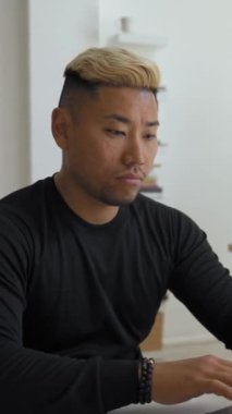 Asyalı adam, modern ofis önermelerinde masa başında dizüstü bilgisayarla çalışıyor. Boyalı saçlı odaklı çalışan yeni web sitesini dikey çekimde geliştirdi.