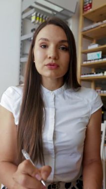 Pozitif bir kadının internetten sipariş alıp ürünlerin detaylarını not defterine yazması. Genç bayan video ile müşteriyle yakın çekim dikey çekim üzerinden iletişim kuruyor..