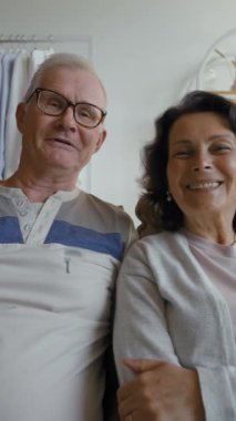 Kıdemli gri saçlı adam ve kadının görüntülü görüntüsü video kamerayla arkadaşlarıyla komik anları tartışıyor. Mutlu çiftler evdeki kanepede oturup dikey çekim yaparlar..