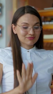 Kadın gözlük takıp dizüstü bilgisayarı açıyor ve raflarda ürünlerle oturuyor. Genç bayan video çekiminde müşteriyle konuşmaya başladı..