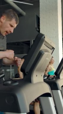 Modern bir spor kulübünün penceresinin yanındaki koşu bandında antrenman yapan ve koşan bir grup sporcu. Yan geniş görünüm dikey çekim.