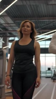 İki sporcunun yavaş çekimde antrenman yapmasının ön görüntüsü. Güçlü kaslı beyaz erkek ve kadınlar boş spor salonuna giriyor. Dikey çekim.