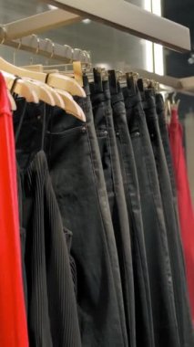 Elbiseli, pantolonlu ve gömlekli askılar mağazada. Yavaş çekim el kamerası atışı. Dikey çekim.