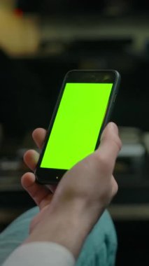 Berber dükkanında kanepede otururken akıllı telefondan berbere kromatonla saç kesimi örneği gösteren isimsiz müşterinin sağ görüşünü yansıt. Dikey çekim.