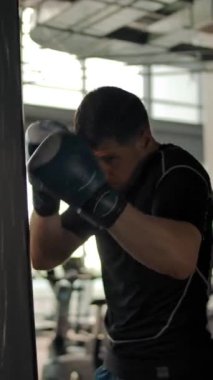 Spor salonunda kum torbasına vuran saldırgan, beyaz bir adamın yakın çekimi. Yavaş çekim kamerası sorunsuz hareket eder. Dikey çekim.