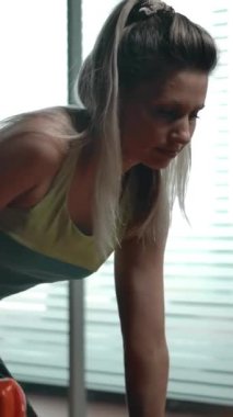 Spor sıralarında diz çökmüş triseps egzersizi yapan seksi kadın. Dikey kamera yüz ve bacaklardan aşağı doğru kayar. Modern jimnastik salonu. Dikey çekim.