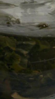 Çaydanlıkta meyve ve çiçekle ahşap bir masada çayı karıştırmak. Şeffaf çaydanlığın yavaş çekim dikey görüntüsü.