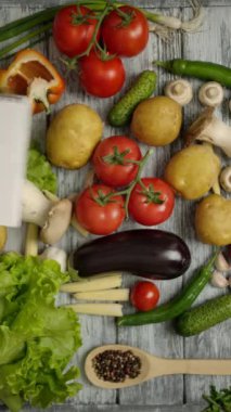 El masanın üzerine sebzeli bir not defteri atar. Domatesler, patatesler, salatalıklar, baklagin ve diğer sebzeler ahşap bir köyün gri masasında yatıyor. Dikey çekim.