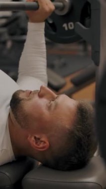 Güçlü bir adam halterle ağırlık kaldırıyor. Kas sporları eğitmeni modern bir spor salonunda güç antrenmanı yapıyor. Dikey çekim.