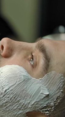 Modern berber dükkanında tıraş olmadan önce siyah eldivenli kadın berber yanak ve boynuna köpük sürmek için fırça kullanıyor. Dikey çekim.