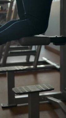 Beyaz adam spor salonundaki gravitron üzerinde barfiks egzersizi yapıyor. Tepeden tırnağa dikey manzara, gövde, yüz, orta plan. Dikey çekim.