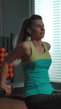 Spor salonundaki çekici kadın triseps egzersizleri yapıyor, kollarını bankta büküyor, kalçalarını yere indiriyor. Birçok kez tekrarlanmış, ağır çekim, modern beden eğitimi. Dikey çekim.