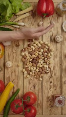 Tahta masada taze sebze ve baharatlarla fındık taşıyan insan elinin tepetaklak olması. Sağlıklı yiyecekler. Dikey çekim.