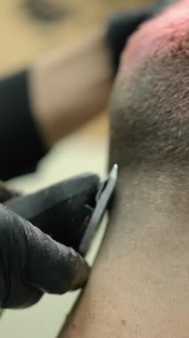 Pembe saçlı bir müşterinin kafasında saç kesme makinesiyle yakın çekim. Siyah eldivenli usta berber otantik bir berber dükkanında kaliteli bir saç tıraşı yapar. Makro yavaş çekim