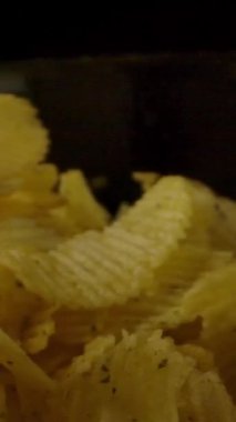 Kaburgalı taze patates cipsi karanlık odada dönen kaseye düşüyor. Dikey çekim.