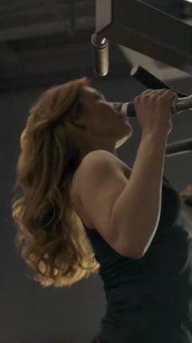 Spor salonunda egzersiz makinesiyle barfiks çeken kaslı güzel bir kızın portresi. El kamerasıyla ateş edilmiş. Sağlıklı yaşam tarzı konsepti. Dikey çekim.