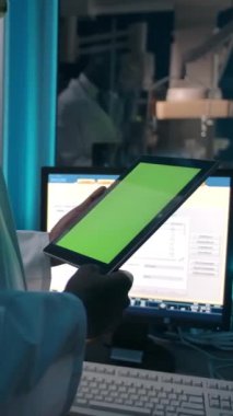 Laboratuvarda çalışırken beyaz bornozlu Afrikalı bir adamın bilgisayarlı masasının yanında durup krom ekranlı tableti incelediğini düşünün. Dikey çekim.