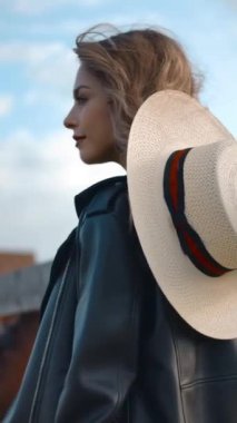 Şapkalı trend bir bayanın ağır çekimde başını çevirmesi ve çiftlikte at kaplamasının yanında dururken omzunun üzerinden gülümseyerek kameraya bakması. Dikey çekim.
