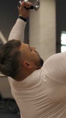 Güçlü bir adam göğüs kasları ve üst bloktaki kaslar üzerinde egzersiz yapıyor. Beyaz tenli güçlü kaslı erkek, panoramik çekim, etrafta uçan kamera. Arka orta görünüm dikey çekim.